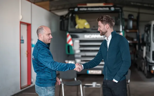 Bese Media zu Besuch beim Partnerbetrieb: Handschlag in der Fahrzeughalle vor dem Saug- und Spülfahrzeug