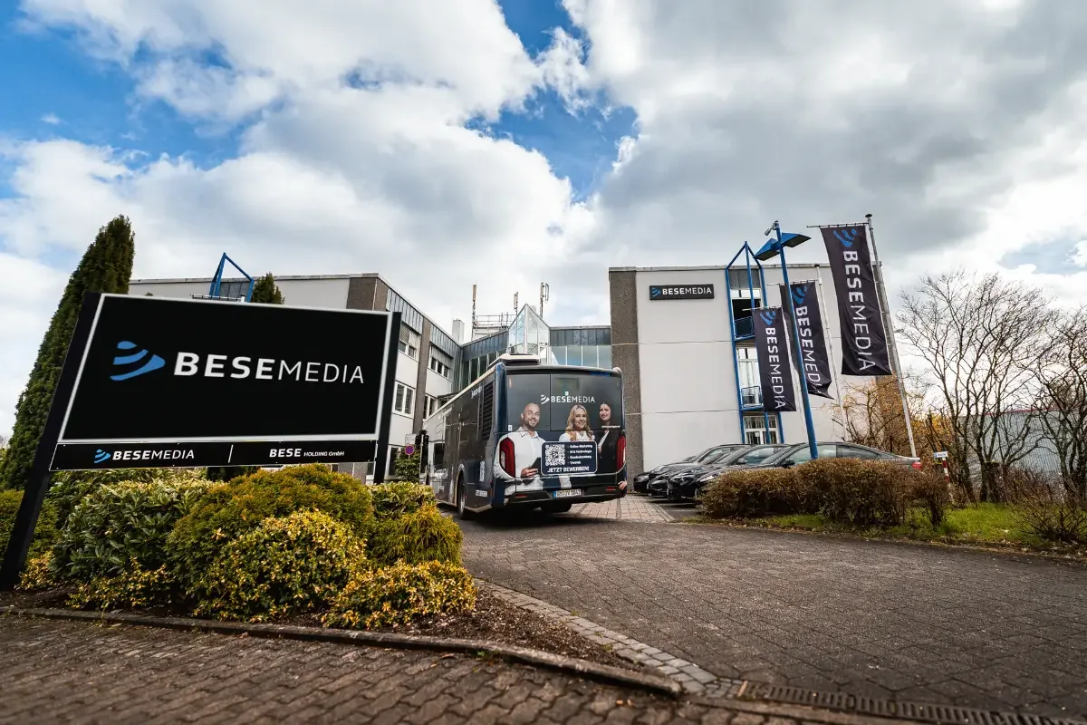 Firmensitz der Bese Media GmbH in Wiehl mit Firmenschild, Flaggen und dem Bese-Bus vor dem Gebäude